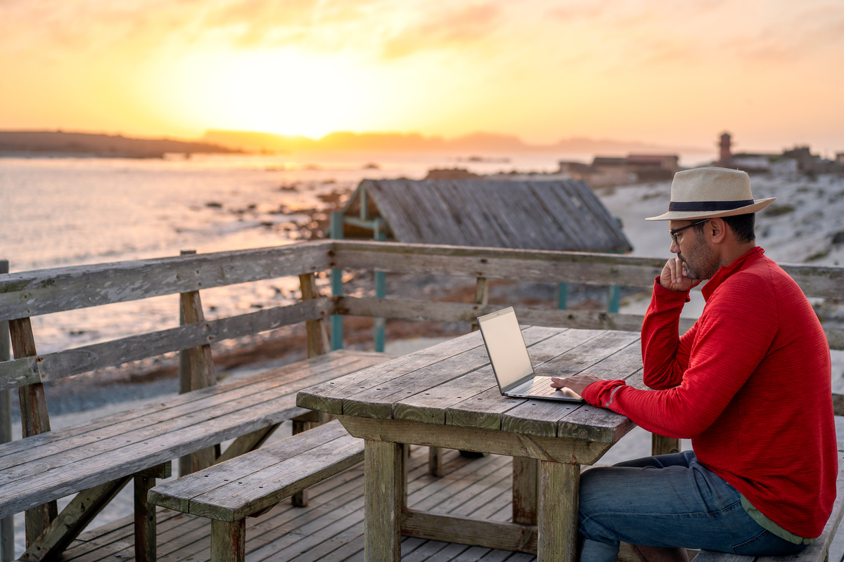 digital nomad sitting outdoor on the beach with a laptop